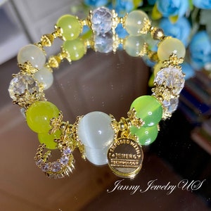 Op de afbeelding: Een gouden armband met groene, witte en heldere kralen. De armband heeft een gouden bedel met de tekst "Infused with I-Energy Technology".