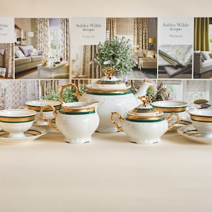 Może przedstawiać: Biały zestaw do herbaty z pozłacanymi i zielonymi zdobieniami. Zestaw zawiera czajnik, dzbanek do śmietanki, cukiernicę i cztery filiżanki do herbaty z talerzykami.