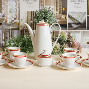 Può includere: Un set da tè in porcellana bianca con finiture rosse e dorate. Il set comprende una teiera, una zuccheriera e sei tazze e piattini.