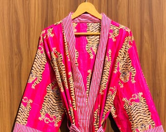 May include: A vibrant pink robe with a tiger print and a striped trim. The robe is made of a lightweight fabric and has a matching belt. The tiger print features orange and black stripes on a pink background. The robe is hanging on a wooden hanger.