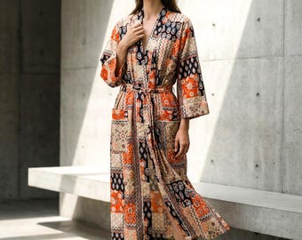 May include: A long, patterned robe in shades of orange, black, and beige. The robe features a patchwork design with a matching belt and pockets. The sleeves are three-quarter length. The robe is worn with black sandals.