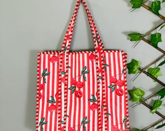 May include: A red and white striped tote bag with a cherry pattern. The bag has a rectangular shape with matching red and white striped handles. The cherry pattern includes red cherries and green leaves.