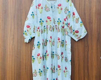 May include: A light blue dress with vertical white stripes and a floral pattern of red, pink, and blue flowers. The dress has short sleeves and is hanging on a wooden hanger.