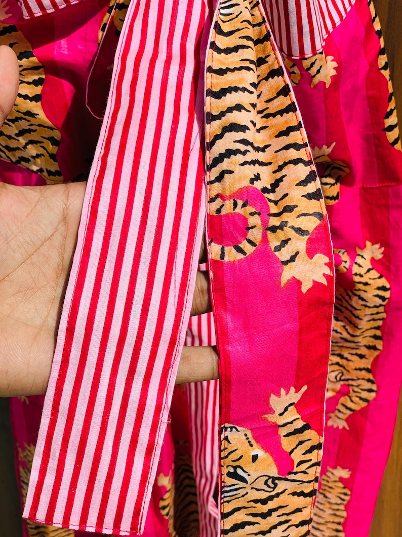 May include: Close-up of a vibrant pink fabric with a tiger stripe pattern and red and white striped ribbon. The tiger stripes are in shades of orange and black. The fabric is likely used for clothing or accessories.