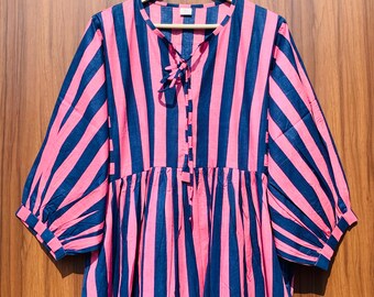 May include: A pink and navy blue striped dress with a round neckline and three-quarter sleeves. The dress features a tie detail at the neckline and a gathered waist. The dress is hanging on a wooden hanger.