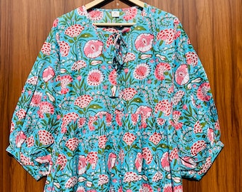May include: A light blue dress featuring a repeating floral pattern in shades of pink, white, and green. The garment has a round neckline with a tie closure, three-quarter length puff sleeves, and a loose, tiered silhouette with an XL size tag.