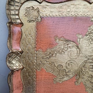 May include: A square, decorative tray with a raised, ornate design. The tray is made of wood and has a pink and gold finish.