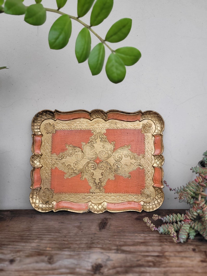 May include: A decorative tray with a scalloped edge and a gold and orange design. The tray has a floral pattern with intricate details.