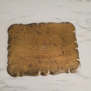 May include: A gold-colored wooden tray with a scalloped edge and a decorative pattern. The tray has a worn, antique look.