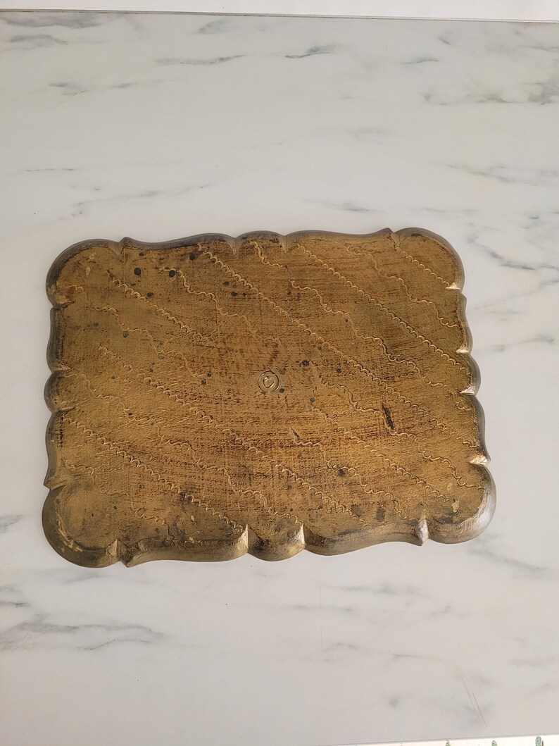 May include: A gold-colored wooden tray with a scalloped edge and a decorative pattern. The tray has a worn, antique look.
