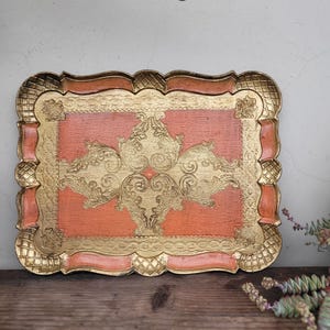 May include: A decorative tray with a scalloped edge and a gold and peach color scheme. The tray features an intricate gold design on the peach background.