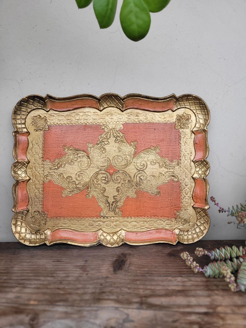 May include: A decorative tray with a scalloped edge and a gold and peach color scheme. The tray features an intricate gold design on the peach background.