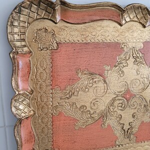 May include: A vintage tray with a pink painted surface and gold leaf accents. The tray has a decorative, ornate design with a scalloped edge.