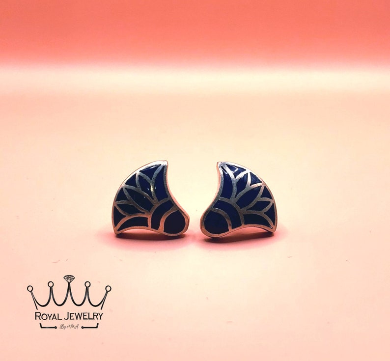 May include: A pair of silver earrings with a blue enamel design. The design is a stylized flower with a silver outline.