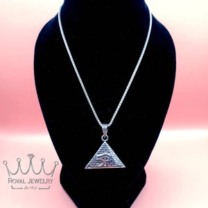 May include: Silver chain necklace with a silver pyramid pendant featuring the Eye of Horus. The necklace is displayed on a black velvet stand.