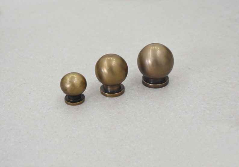 May include: Three brass cabinet knobs of varying sizes. The knobs are round and have a smooth, polished finish.