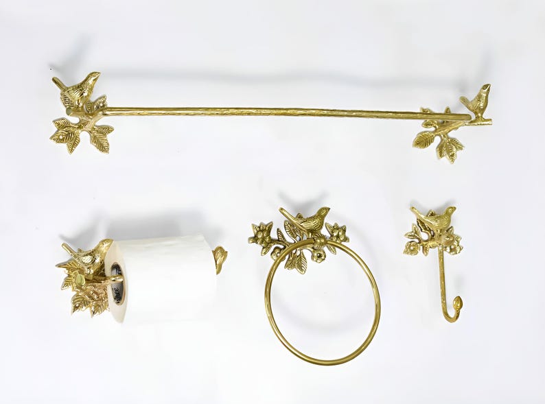 Op de afbeelding: Gouden badkamerset met een handdoekrek, toiletpapierhouder, handdoekring en haak. Elk onderdeel heeft een decoratief vogeltje dat op een tak met bladeren zit.