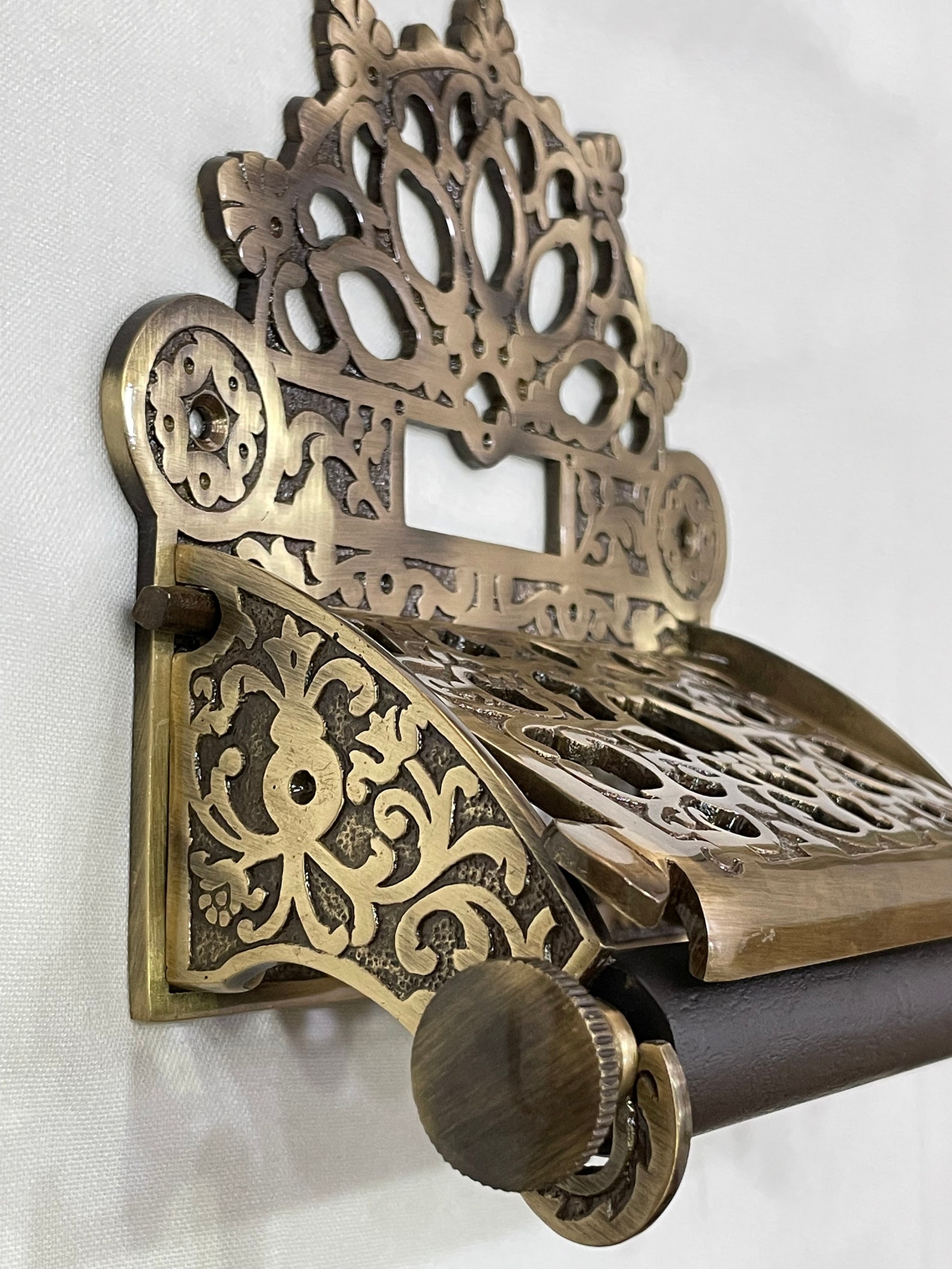 Close-up of ornate Victorian brass toilet paper holder with detailed floral and lattice engraving
