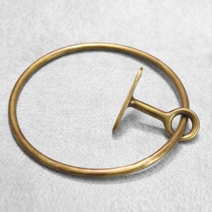 May include: A brass towel ring with a hook on the side. The ring is round and the hook is shaped like a T.