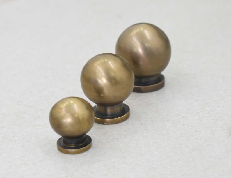 May include: Three brass cabinet knobs of varying sizes. The knobs are round and have a smooth, polished finish.