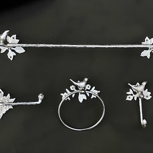 Peut inclure: Un ensemble de salle de bain en argent avec une barre &agrave; serviettes, un porte-papier toilette, un anneau &agrave; serviettes et un crochet. Chaque pi&egrave;ce pr&eacute;sente un oiseau d&eacute;coratif perch&eacute; sur une branche.