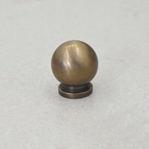 May include: A round, brass knob with a smooth, shiny finish. The knob has a small, flat base.