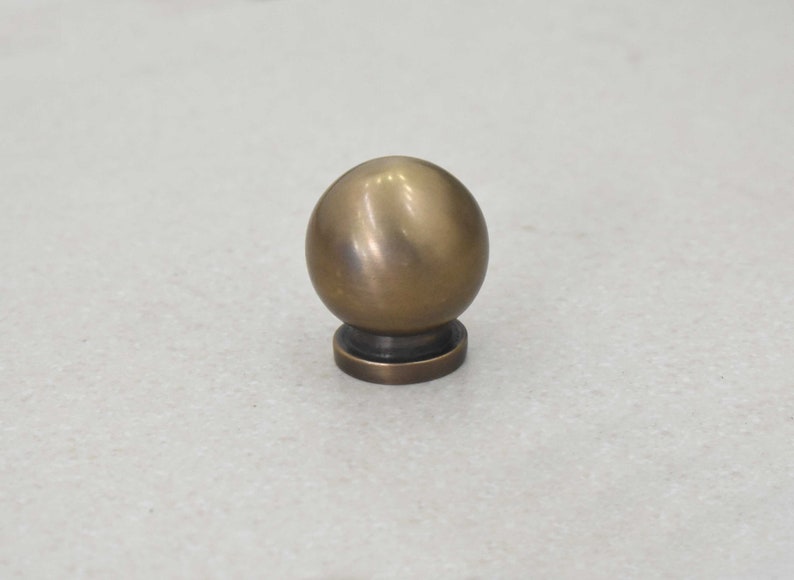 May include: A round, brass knob with a smooth, shiny finish. The knob has a small, flat base.