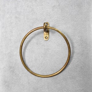 May include: A brass towel ring with a simple, circular design. The ring is mounted to a wall with a single screw.