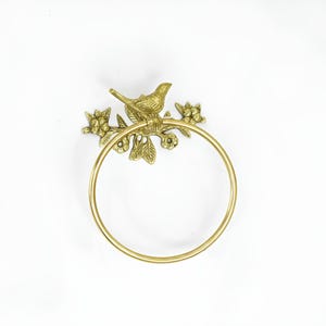 Op de afbeelding: Gouden metalen handdoekring met een vogel die op een tak zit met bladeren en bloemen.