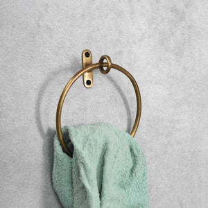 May include: A brass towel ring with a simple, circular design. The ring is mounted to a wall and has a towel draped over it.