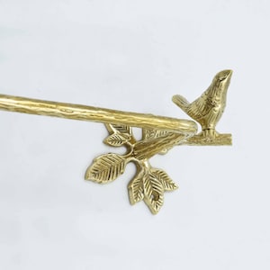 Op de afbeelding: Gouden metalen handdoekrek met een vogel die op een tak met bladeren zit. Het rek is ontworpen om een handdoek te houden.