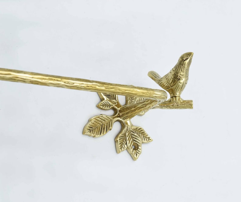 Op de afbeelding: Gouden metalen handdoekrek met een vogel die op een tak met bladeren zit. Het rek is ontworpen om een handdoek te houden.