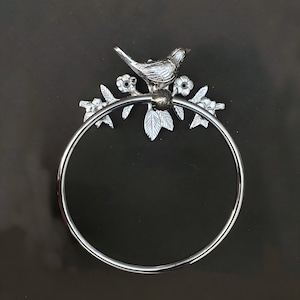 May include: Silver metal towel ring with a bird and floral design. The ring is circular and the design is attached to the top of the ring.