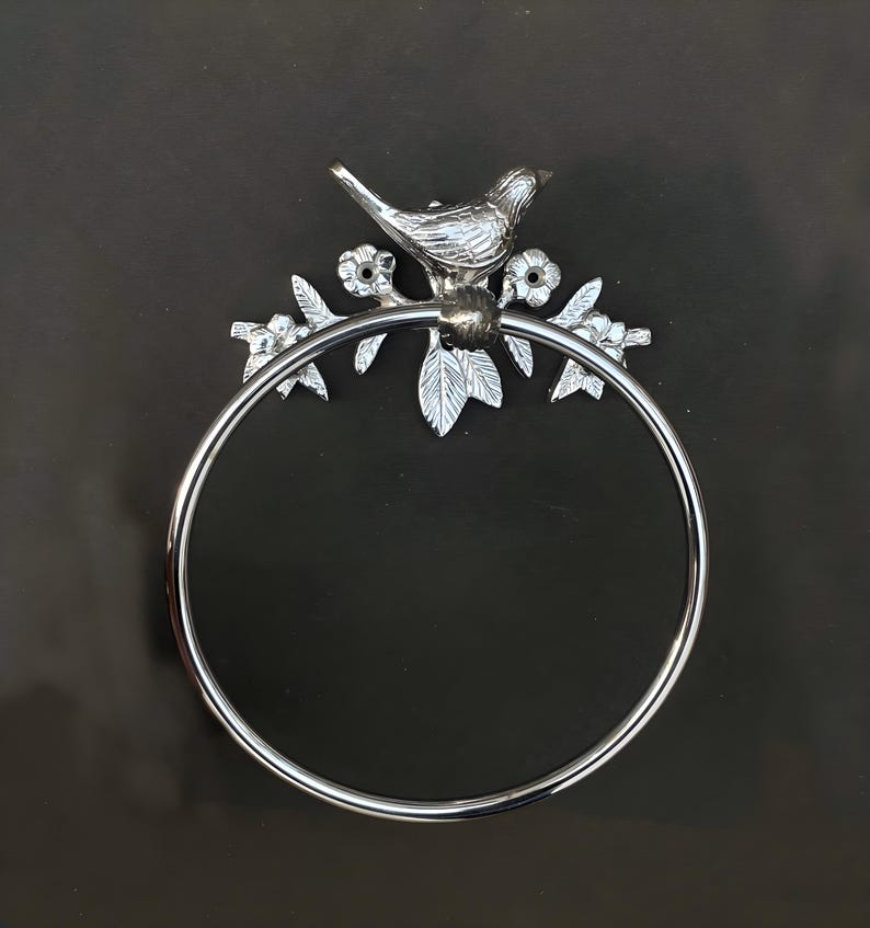 May include: Silver metal towel ring with a bird and floral design. The ring is circular and the design is attached to the top of the ring.