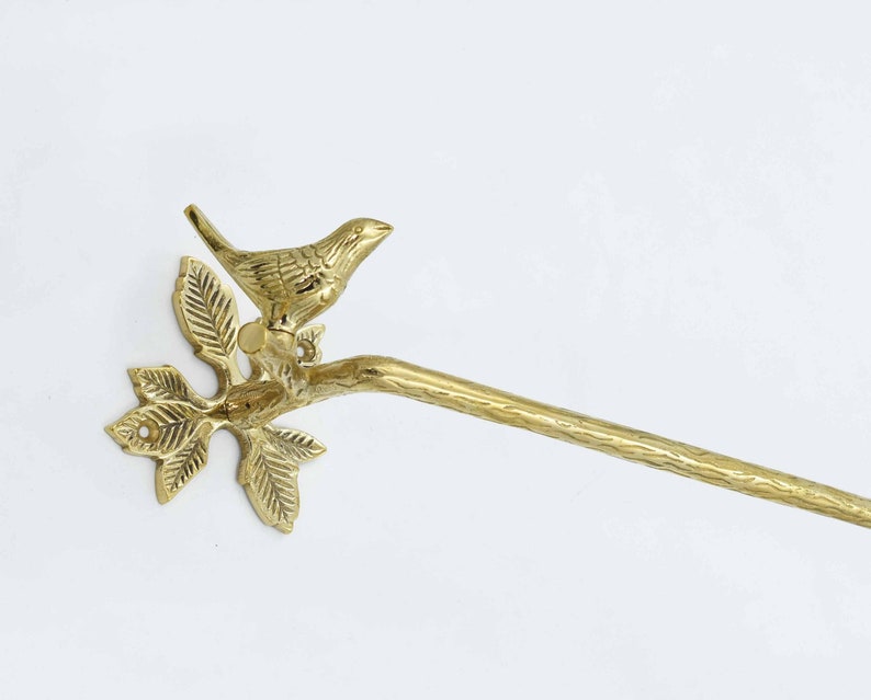 Op de afbeelding: Gouden metalen handdoekhouder met een vogel die op een tak met bladeren zit. De tak is bevestigd aan een wandbevestiging.