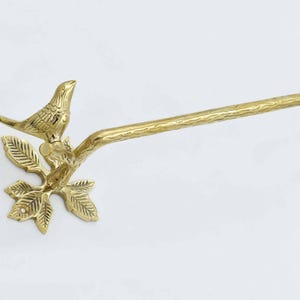 Op de afbeelding: Gouden metalen handdoekhouder met een vogel op een tak. De stang is aan een muur bevestigd.