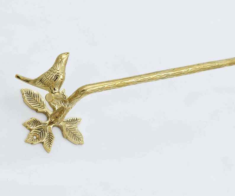 Op de afbeelding: Gouden metalen handdoekhouder met een vogel op een tak. De stang is aan een muur bevestigd.