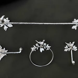 May include: Silver bathroom hardware set with a towel bar, a toilet paper holder, a towel ring, and a hook. Each piece features a decorative bird perched on a branch.