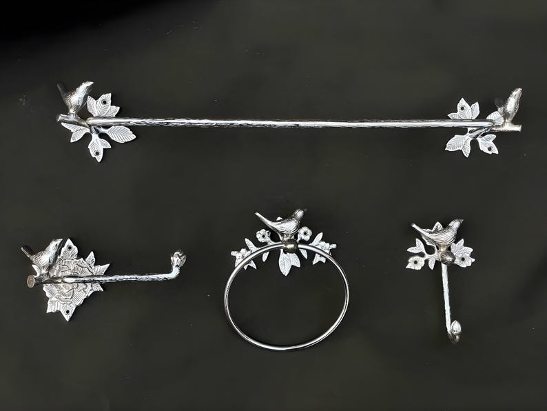 May include: Silver bathroom hardware set with a towel bar, a toilet paper holder, a towel ring, and a hook. Each piece features a decorative bird perched on a branch.
