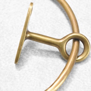 May include: A brass towel ring with a simple, rounded design. The ring is attached to a wall mount with a single screw.