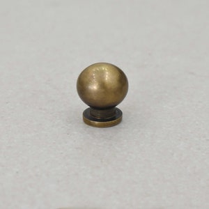 May include: A round, brass knob with a smooth, shiny finish. The knob has a small, round base.