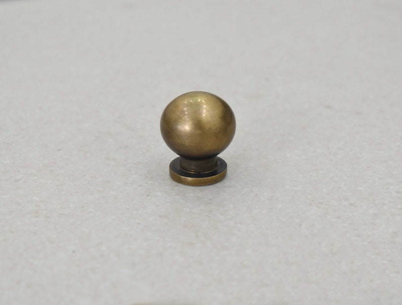 May include: A round, brass knob with a smooth, shiny finish. The knob has a small, round base.