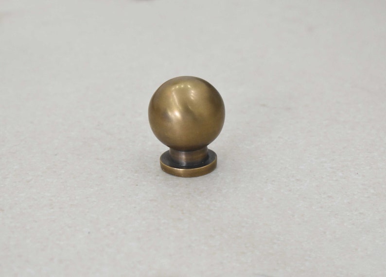 May include: A round, brass knob with a smooth, slightly textured surface. The knob has a small, flat base.