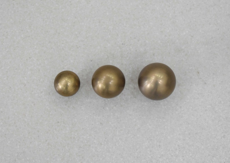 May include: Three round, metallic, gold-colored knobs of different sizes.