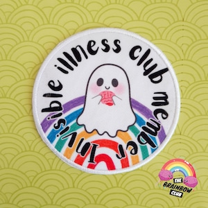 Pode incluir: Etiqueta redonda branca bordada com um arco-íris e um fantasma segurando um cérebro. O texto na etiqueta diz "Invisible illness club member".