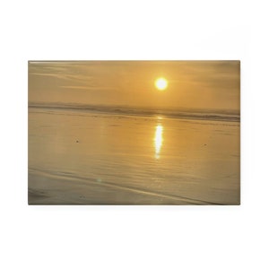 Puede incluir: Impresión en lienzo que representa una escena de playa al atardecer. El sol es un orbe amarillo brillante, que se refleja en la arena mojada y el océano. El cielo es de un color dorado suave, y las olas rompen suavemente.