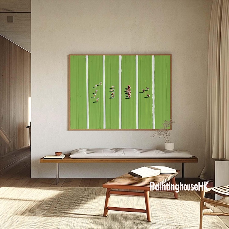 May include: A framed print of an aerial view of a green field with white lines and red figures. The print is hanging on a white wall above a wooden bench.