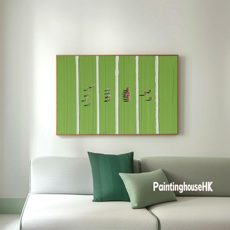 May include: A green and white abstract painting depicting a field with white lines and small red and green figures. The painting is framed and hanging on a white wall above a light gray couch with green and light green throw pillows. The text 