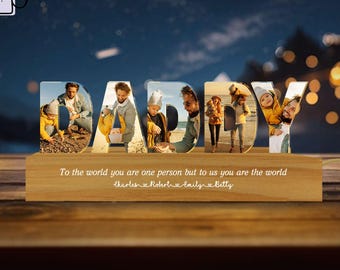 May include: A wooden block with the word "DADDY" in large, clear letters. Each letter holds a family photo. The base of the block has the text "To the world you are one person but to us you are the world".