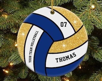 May include: A white, blue, and gold volleyball ornament with glitter. The ornament has the text "YOUR TEAM VOLLEYBALL" and "THOMAS" on it. The number "07" is also on the ornament.